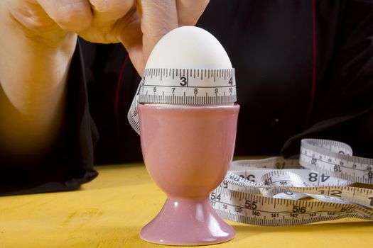 Egg in the holder and hands of the cook with a tape measure