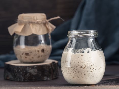 Active wheat and rye sourdough starter in glass jar on brown wooden background. Starter for sourdough bread. Toned image. Copy space.