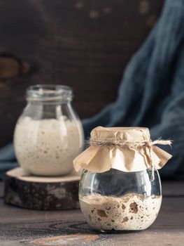 Active rye and wheat sourdough starter in glass jar on brown wooden background. Starter for sourdough bread. Toned image. Copy space. Vertical