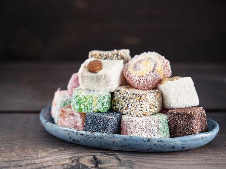 Closeup view of assortment turkish delight in blue trandy plate on dark wooden background. Copy space. Low key