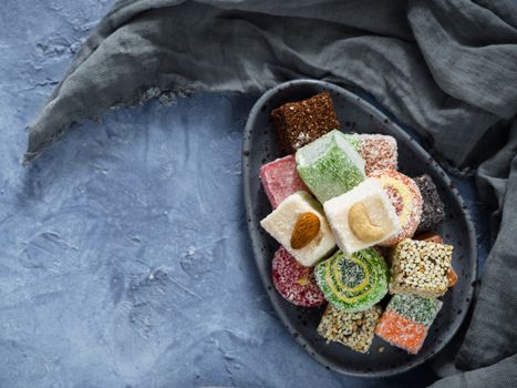 Turkish delight on blue concrete background. Assortment of traditional easten sweet dessert in trandy blue plate. Selective focus. Top view or flat lay. Copy space.