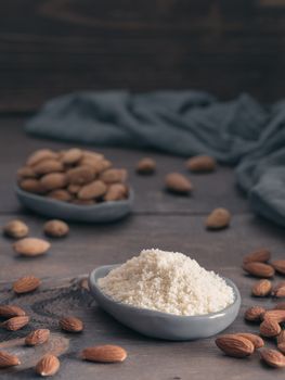Almond powder in gray trendy plate and almonds on dark wooden table. Almond flour and peeled kernel almonds. Copy space. Vertical.