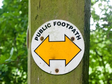 white circle on wooden post with public footpath and yellow arrow