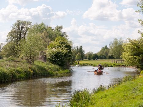 people rowing boats down the river stour in dedham essex uk england in constable country relaxing outside in sun