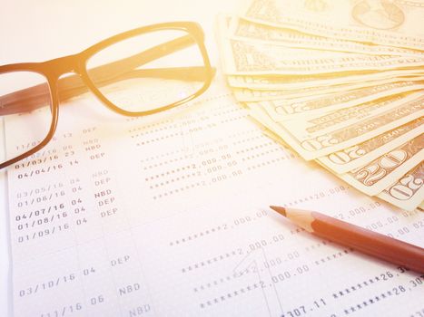 Business, finance, savings, banking or  loan concept : Pencil, eyeglasses, money and savings account passbook or financial statement on white background