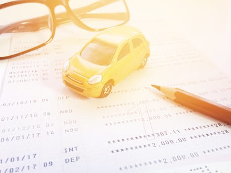 Business, finance, savings, banking or car loan concept : Miniature car model, pencil, eyeglasses and savings account passbook or financial statement on white background