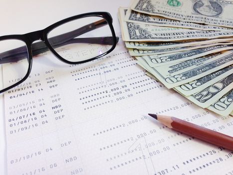 Business, finance, savings, banking or  loan concept : Pencil, eyeglasses, money and savings account passbook or financial statement on white background