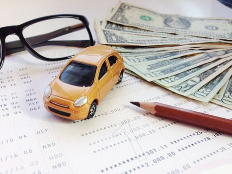 Business, finance, savings, banking or car loan concept : Miniature car model, pencil, eyeglasses, money and savings account passbook or financial statement on white background