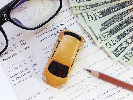 Business, finance, savings, banking or car loan concept : Miniature car model, pencil, eyeglasses, money and savings account passbook or financial statement on white background