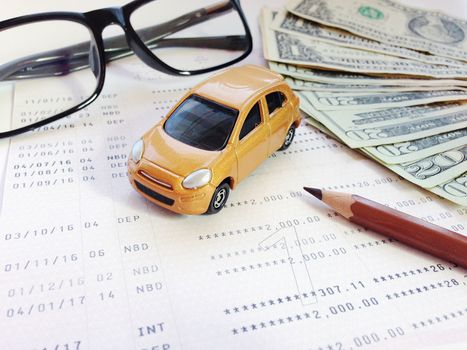 Business, finance, savings, banking or car loan concept : Miniature car model, pencil, eyeglasses, money and savings account passbook or financial statement on white background