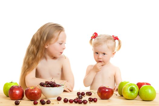 two little girls eat fruit at a table on the isolated background