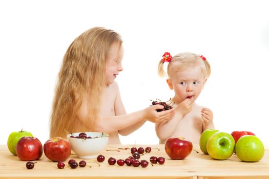 two little girls eat fruit at a table on the isolated background