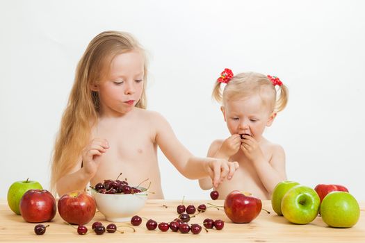 two little girls eat fruit at a table on the isolated background