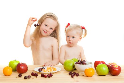 two little girls eat fruit at a table on the isolated background