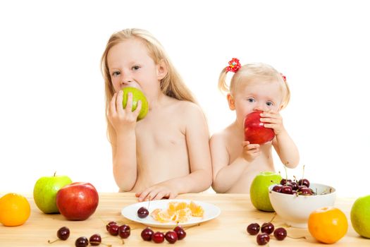 two little girls eat fruit at a table on the isolated background