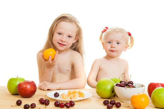 two little girls eat fruit at a table on the isolated background