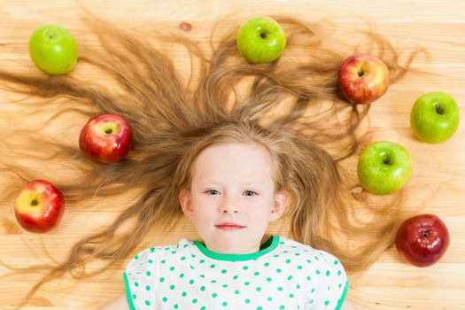 the little girl among apples on a wooden background