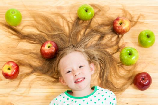 the little girl among apples on a wooden background