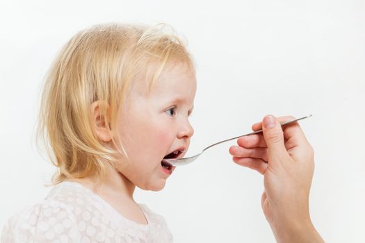 the little girl is spoon-fed on the isolated background