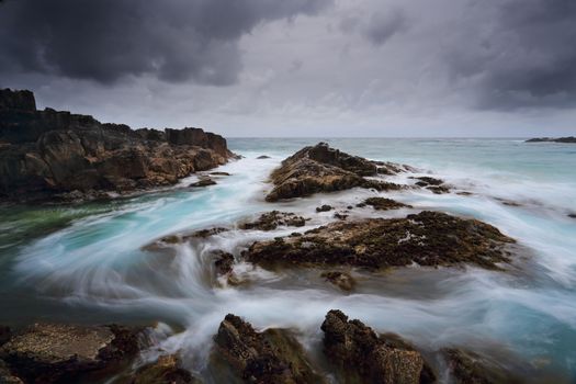 Heavy storm clouds loom overhead as fast flowing water moves swiftly through the channel.  Location Meringo, Australia