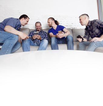 Four happy male friends using their mobile phones sitting on a sofa at home