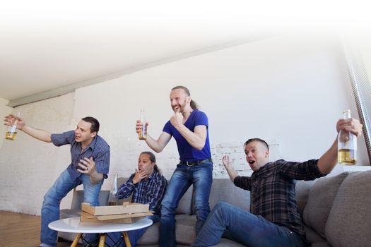 Male friends sports fans watching winning football match on TV at home celebrating winning goal huddled on couch shouting excited sharing snacks drinking beer