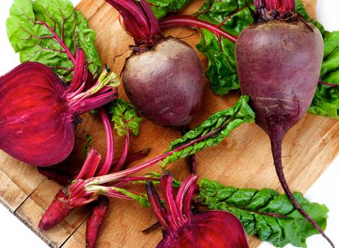 Arrangement of Fresh Raw Organic Beet Roots Full Body, Halves and Young Sprouts with Green Beet Tops closeup on Wooden Cutting Board. Top View 