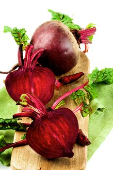 Two Halves and One Full Body Fresh Raw Organic Beet Roots with Green Beet Tops on Wooden Board and Napkin isolated on White background