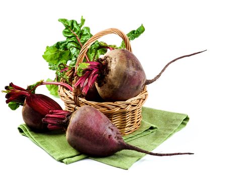 Arrangement of Full Body and Half of Fresh Raw Organic Beet Roots with Green Beet Tops in Wicker Basket on Napkin isolated on White background