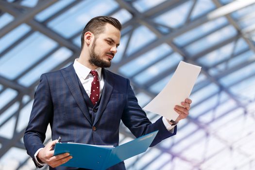 Portrait of mature businessman holding binder and documents over modern building interior background