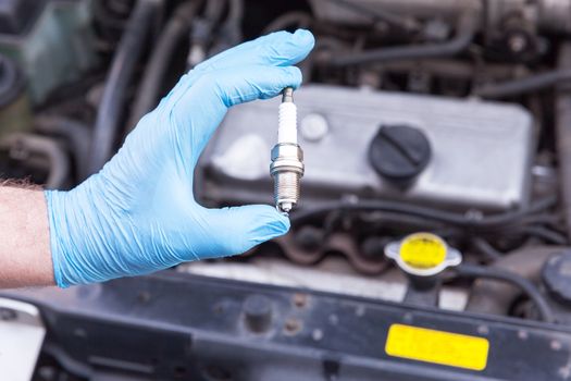 Auto mechanic wearing protective work glove holds new spark plug over a car engine