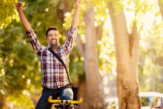 Casual smiling businessman ride a bike and celebrates success with open arms.