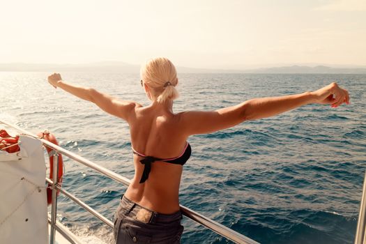 Rear view of a beautiful young woman enjoying at cruise with raised arms. Looking for away.