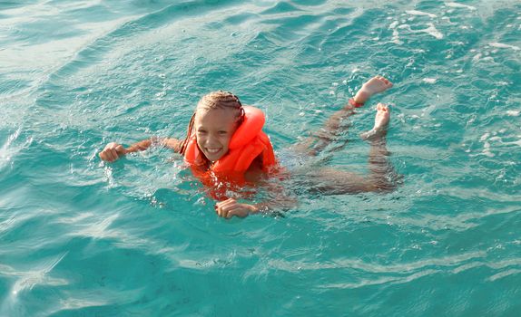 Cute smiling little girl with swim vest enjoying and relaxed swimming in the sea. 