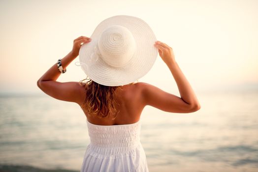 Rear view of a beautiful woman in white dress and white summer hat.