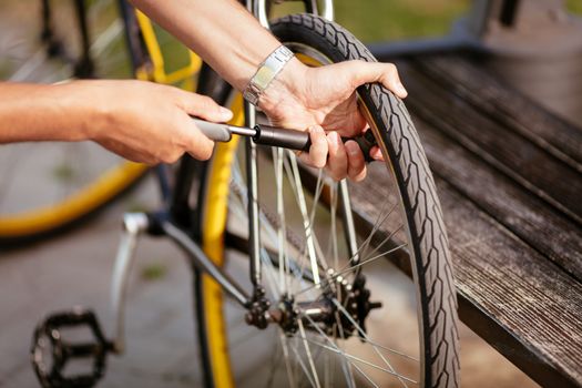 Close-up of a man pumping bicycle wheel on the street.