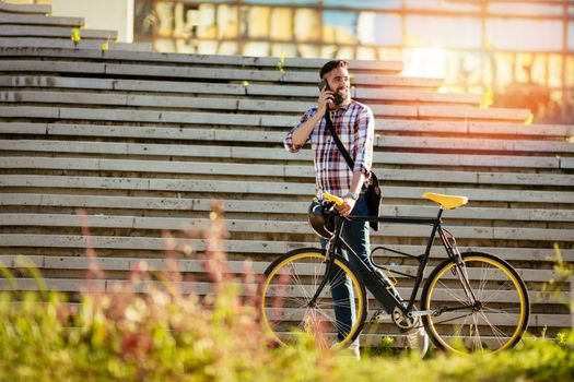 Casual businessman going to work by bicycle. He is pushing bike and using phone.