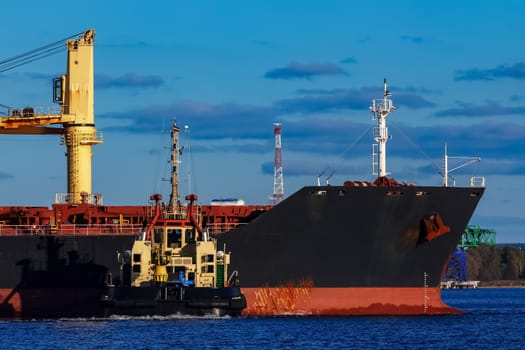 Black cargo ship mooring at the port with tug ship support