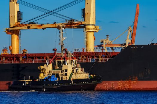 Black cargo ship mooring at the port with tug ship support