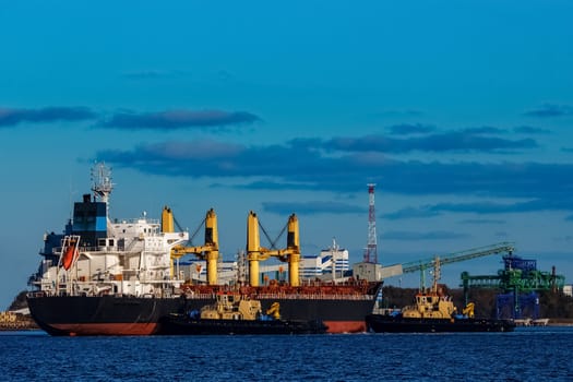 Black cargo ship mooring at the port with tug ship support