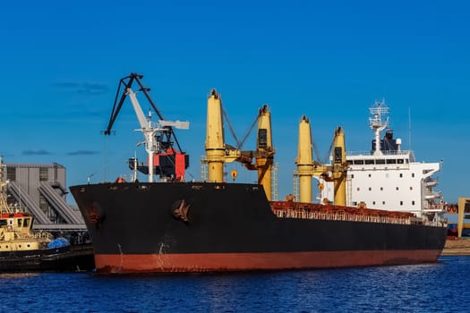Black cargo ship mooring at the port with tug ship support