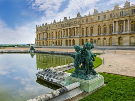 Part of a northwest facade of the Central gallery of the Palace of Versailles with Water Parterre and sculpture "One child and two loves" in the foreground, France
