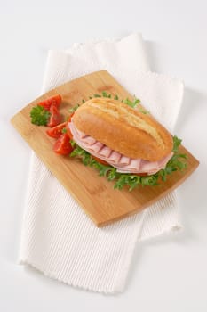 crusty roll sandwich with ham on wooden cutting board