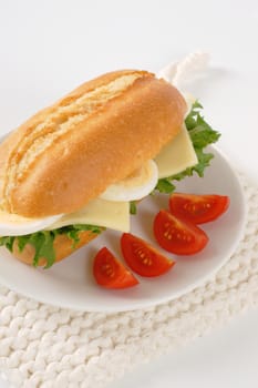 crusty roll sandwich with eggs and cheese on white plate