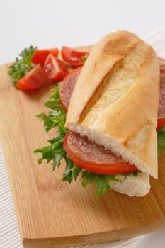 French loaf sandwich with salami on wooden cutting board