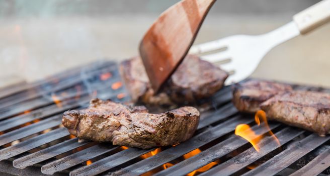 Chef grilling a beef steak on open flame BBQ.