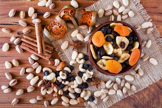 Mix of dried fruits in a wooden bowl and nuts over a rustic table seen from above