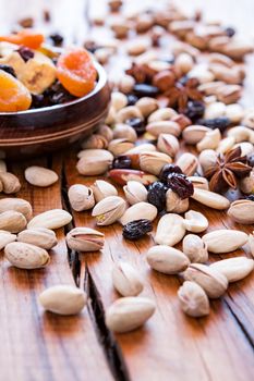 Mix of dried fruits in a wooden bowl and nuts over a rustic table in backlit