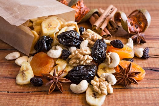 Closeup of mix of dried fruits and nuts in a paper bag over a rustic table