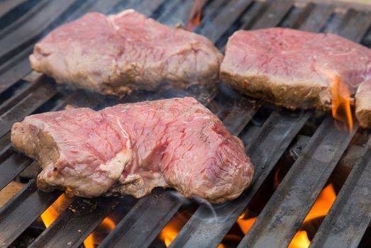 Raw beef steaks on the grill with flames.
